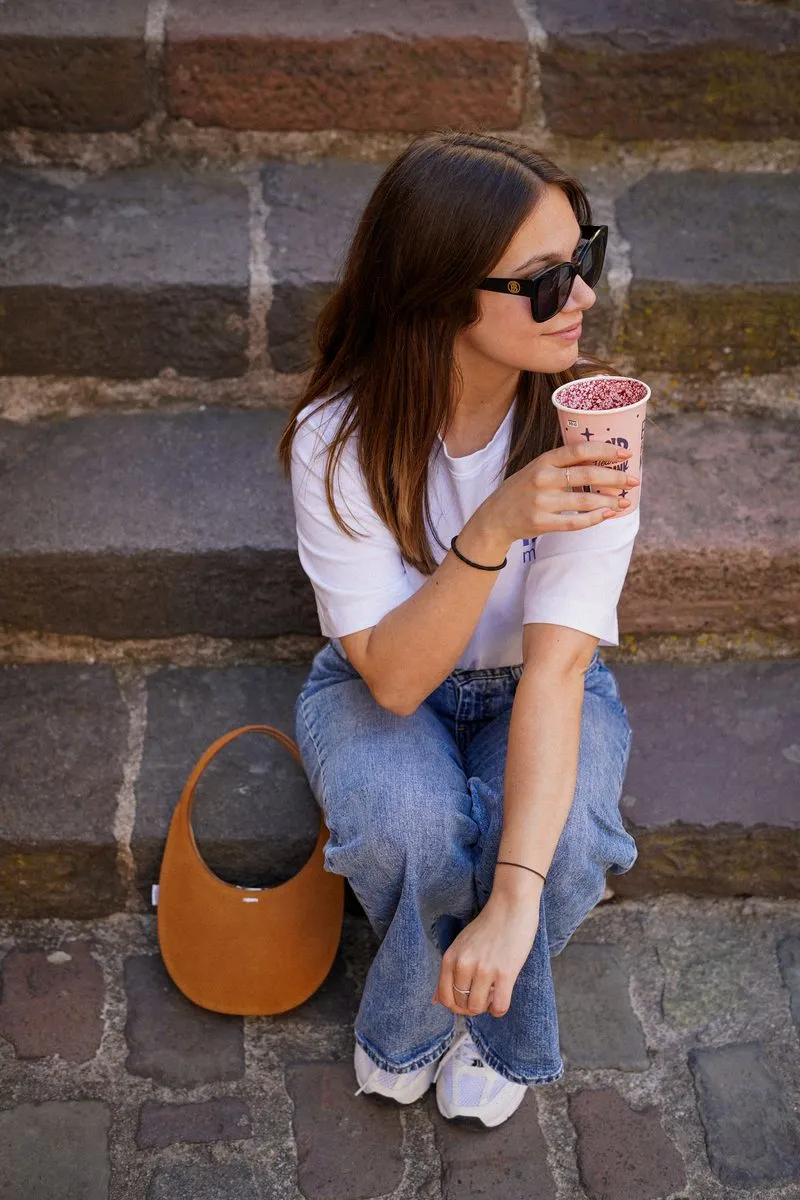 Clémence assise sur des marches en pierre, de profil, avec une boisson