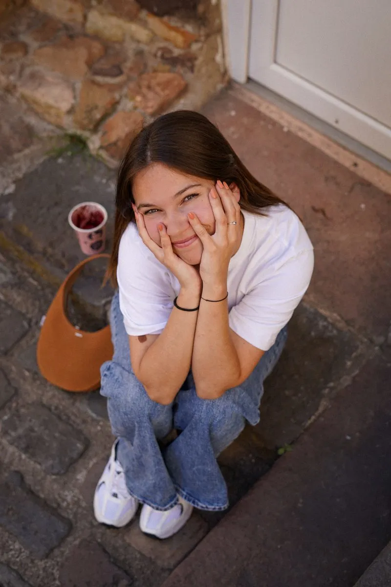 Clémence souriante, assise sur des marches en pierre